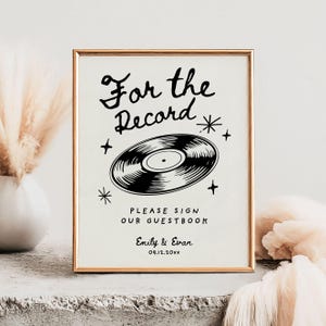 May include: A black and white sign with the text "For the Record" and a vinyl record graphic. The sign also includes the text "Please sign our guestbook" and the names "Emily & Evan" with the date "09.12.20xx".