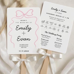 May include: Two white wedding fans with wooden handles and white ribbon bows. One fan features the names "Emily + Evan" with a pink bow design. The other fan lists the ceremony details and wedding party.