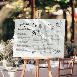 May include: A white sign on a wooden easel features a crossword puzzle with the text "Sip & Solve" and the names "Hannah & Evan." The puzzle includes illustrations of a bride and groom, flowers, and other wedding-related graphics.