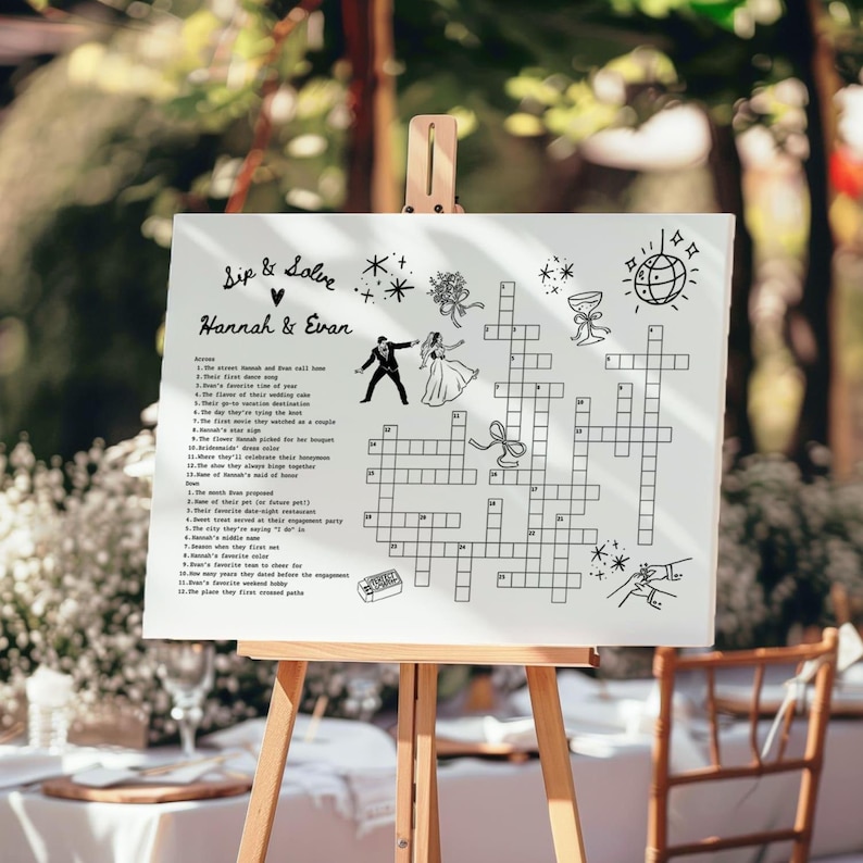May include: A white sign on a wooden easel features a crossword puzzle with the text "Sip & Solve" and the names "Hannah & Evan." The puzzle includes illustrations of a bride and groom, flowers, and other wedding-related graphics.