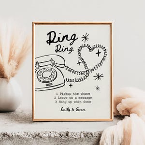 May include: A framed print with a gold border features a retro telephone illustration and the words "Ring Ring." The phone cord forms a heart shape. Text below reads "1 Pickup the phone, 2 Leave us a message, 3 Hang up when done" and the names "Emily & Evan."