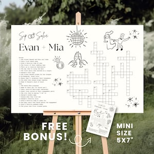 May include: A white wedding crossword puzzle with the names "Evan + Mia" at the top. The puzzle includes illustrations of champagne flutes, a disco ball, and a couple dancing. A smaller, matching puzzle is included.