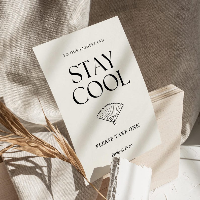 K&ouml;nnte beinhalten: Eine cremefarbene Karte mit den Worten "STAY COOL" in gro&szlig;en schwarzen Buchstaben, einer F&auml;cherillustration und dem Text "PLEASE TAKE ONE!" und "Emily & Evan". Die Karte steht auf einem Holzblock.