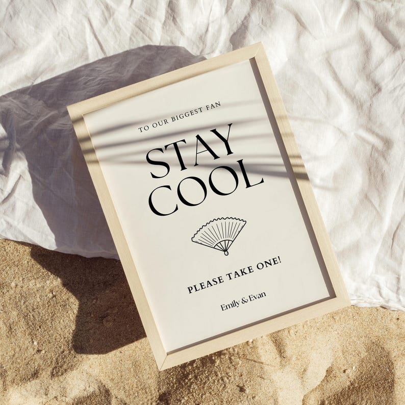 K&ouml;nnte beinhalten: Ein gerahmtes Schild mit dem Text "TO OUR BIGGEST FAN STAY COOL" in Schwarz, zusammen mit einer F&auml;cherillustration. Das Schild enth&auml;lt auch den Text "PLEASE TAKE ONE!" und die Namen "Emily & Evan". Der Rahmen ist hell.