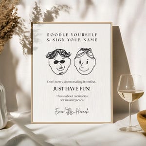 May include: A framed print with the text "DOODLE YOURSELF & SIGN YOUR NAME" and the phrase "JUST HAVE FUN!". The print features two doodle faces and the names "Evan & Hannah" at the bottom.