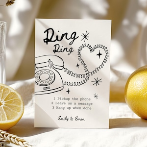 May include: A cream-colored card with a retro phone illustration and the words "Ring Ring." The phone cord forms a heart shape. Text below reads "1 Pickup the phone, 2 Leave us a message, 3 Hang up when done." Names "Emily & Evan" are at the bottom.