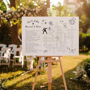 May include: A white sign on a wooden easel with a crossword puzzle design for a wedding. The sign includes the text "Sip & Solve" and the names "Hannah & Evan". The crossword puzzle has illustrations of a couple, a disco ball, and other wedding-related graphics.