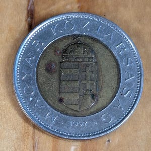 May include: A silver and gold coin with the text "MAGYAR KOZTARSASAG" around the edge and the year "1997" at the bottom. The coin features a coat of arms in the center.