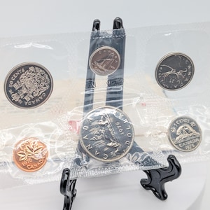 May include: A set of three ceramic mugs with a speckled, matte finish. The mugs are in cream, light grey, and dark grey. Each mug has a simple, minimalist design, ideal for coffee or tea.