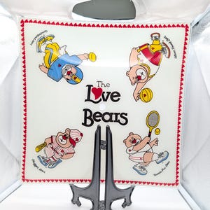 May include: A clear, square decorative plate featuring cartoon bears playing sports. The plate has a red heart border and the words "The Love Bears" in the center. The bears are dressed in sports uniforms.