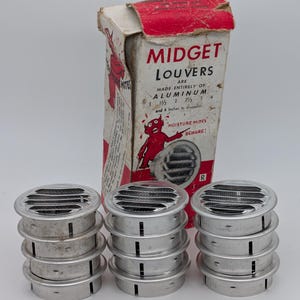 Puede incluir: Un conjunto de rejillas Midget de aluminio, con una caja de cartón con texto e ilustraciones en rojo y blanco. La caja advierte sobre "Moisture Mites". Las rejillas están apiladas en grupos, con una regla en primer plano.