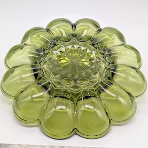May include: A green glass serving dish with a flower-like design. The dish has a central, textured area surrounded by petal-shaped sections. The glass has a slight tint of yellow and is set against a white background.