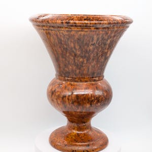 May include: A large, decorative urn with a speckled brown and orange glaze. The urn has a wide, flared top, a bulbous midsection, and a rounded base. It is displayed on a white surface.