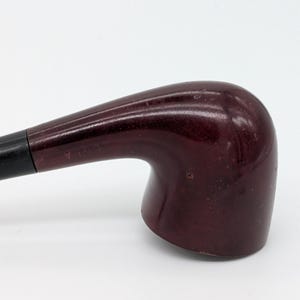 May include: A burgundy smoking pipe with a curved stem and a rounded bowl. The stem is black and connects to the bowl. The pipe is made of wood and has a smooth, polished finish. A classic smoking accessory.