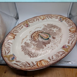 Może przedstawiać: Biały ceramiczny kubek z czarnym uchwytem i napisem "But First, Coffee" pogrubioną, czarną czcionką. Kubek jest umieszczony na rozmytym tle, podkreślając jego czysty design.