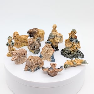 Peut inclure: Une collection de petites figurines en céramique émaillée représentant divers animaux et personnages humains. L'ensemble comprend un chien, un écureuil, un sanglier, un loup, un papillon, un oiseau et plusieurs personnages aux tons terreux.