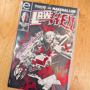 May include: A comic book titled "Pinhead vs. Marshal Law" in a protective sleeve. The cover features a black and red graphic with the title in large, stylized letters. The comic is part 1 of 2, published by Epic Comics.