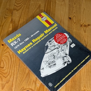 May include: A Haynes Repair Manual for the Mazda RX-7, covering models from 1979 through 1985. The cover features a detailed diagram of the car's internal components. The manual is based on a complete teardown and rebuild, with essential information.