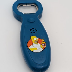 May include: A blue bottle opener with a metal top and a blue plastic handle. The handle features a cartoon image of Homer Simpson holding a Duff beer bottle. The image is on a white and orange background.
