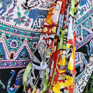 May include: A colorful assortment of fabric bags with unique patterns. One bag features a cityscape design, while others showcase geometric and abstract art. The bags are draped over a patterned textile with deer and floral motifs, creating a vibrant display.