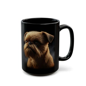 May include: Black ceramic mug with a detailed illustration of a Brussels Griffon dog. The dog is rendered in shades of brown, with a prominent beard and expressive eyes. The mug has a large handle.