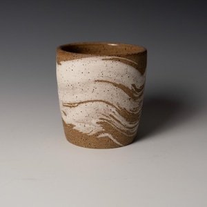 Puede incluir: Un vaso de cerámica hecho a mano con una base marrón moteada y un diseño blanco en espiral. El interior y el borde son marrones. Ideal para café, té u otras bebidas. Una adición elegante a cualquier cocina.