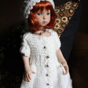 May include: A white knitted dress with a white knitted hat and a pearl necklace. The doll has red hair and blue eyes.