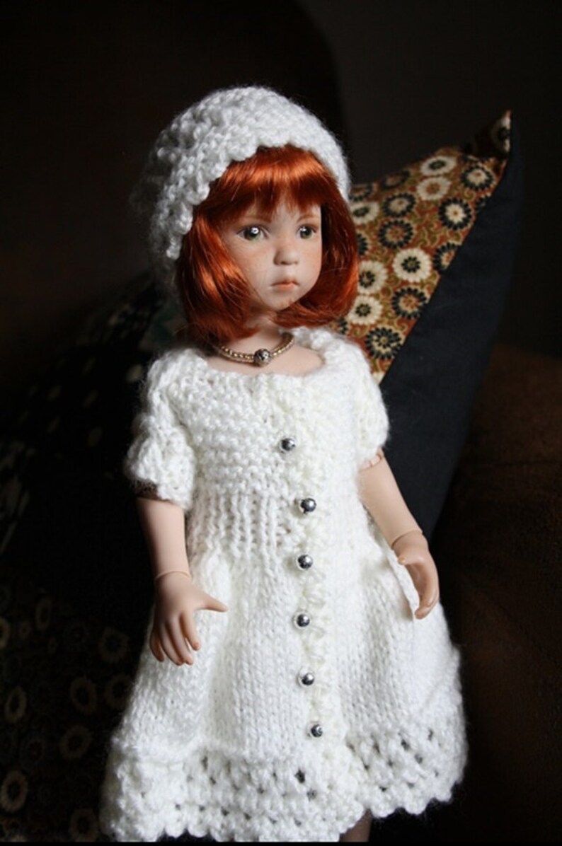 May include: A white knitted dress with a white knitted hat and a pearl necklace. The doll has red hair and blue eyes.