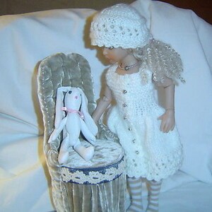 May include: A white crocheted dress with a white crocheted hat and a white bunny rabbit sitting on a plush chair.