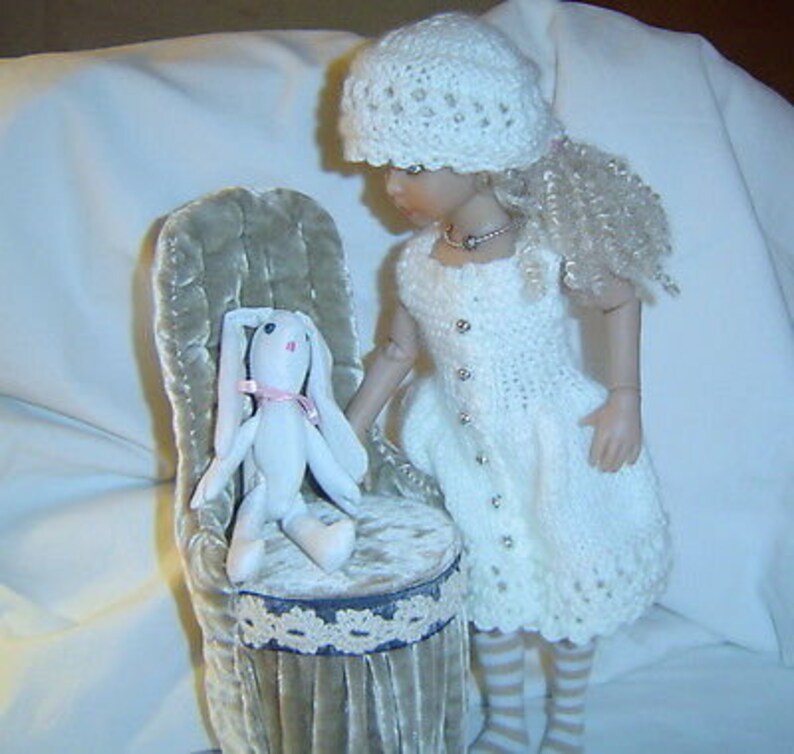 May include: A white crocheted dress with a white crocheted hat and a white bunny rabbit sitting on a plush chair.