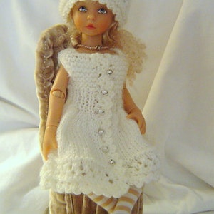 May include: A white porcelain doll wearing a white crocheted dress and hat. The doll is sitting on a brown velvet chair.
