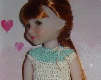 May include: A doll with long, red hair wearing a white crocheted dress with a light blue crocheted collar.