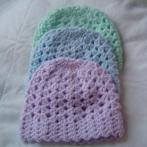 May include: Three crocheted hats in different pastel colors: lavender, light blue, and mint green. The hats are stacked on top of each other, with the lavender hat on the bottom.