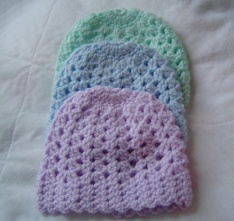May include: Three crocheted hats in different pastel colors: lavender, light blue, and mint green. The hats are stacked on top of each other, with the lavender hat on the bottom.