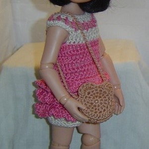 May include: A doll wearing a handmade crochet outfit. The outfit includes a pink and white striped dress, matching hat, purse, and shoes. The hat has a pink flower accent. The doll is standing.