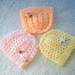 May include: Three crocheted baby hats in pink, peach, and yellow with white flower embellishments.