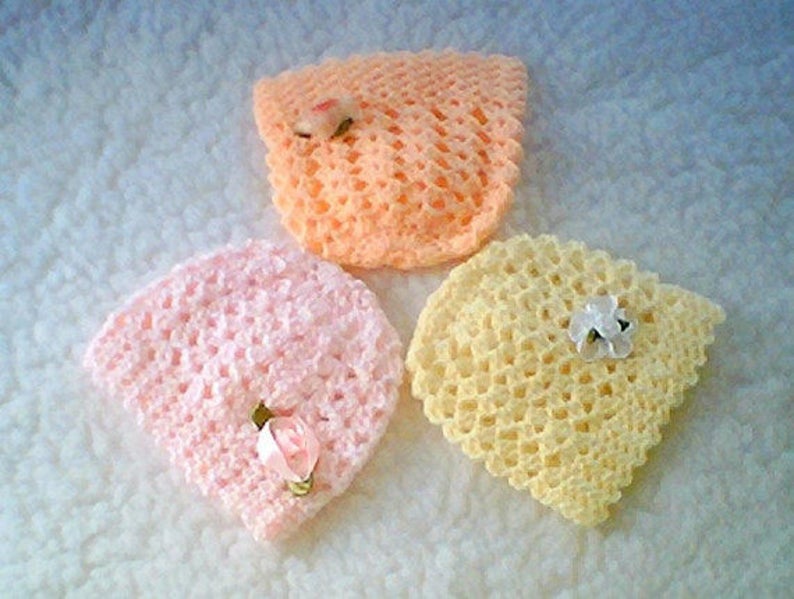 May include: Three crocheted baby hats in pink, peach, and yellow with white flower embellishments.