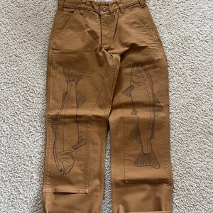 May include: Brown work pants with a cuffed hem and two black fish designs on the legs.