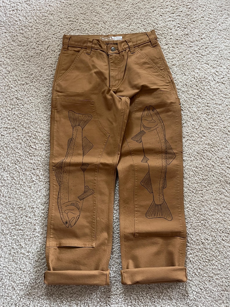 May include: Brown work pants with a cuffed hem and two black fish designs on the legs.
