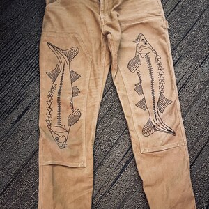 May include: A pair of brown work pants with black sturgeon fish designs on the legs.