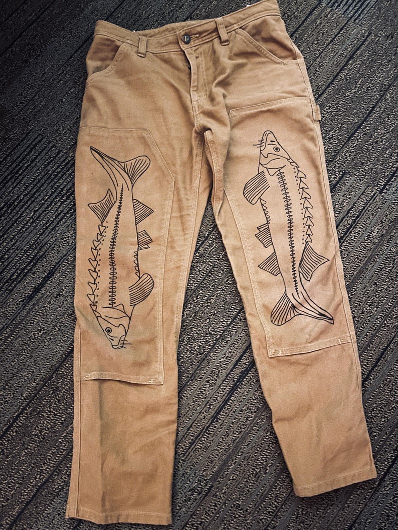 May include: A pair of brown work pants with black sturgeon fish designs on the legs.