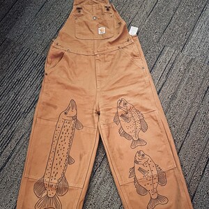 May include: Brown canvas overalls with a white strap and a black fish design on each leg.