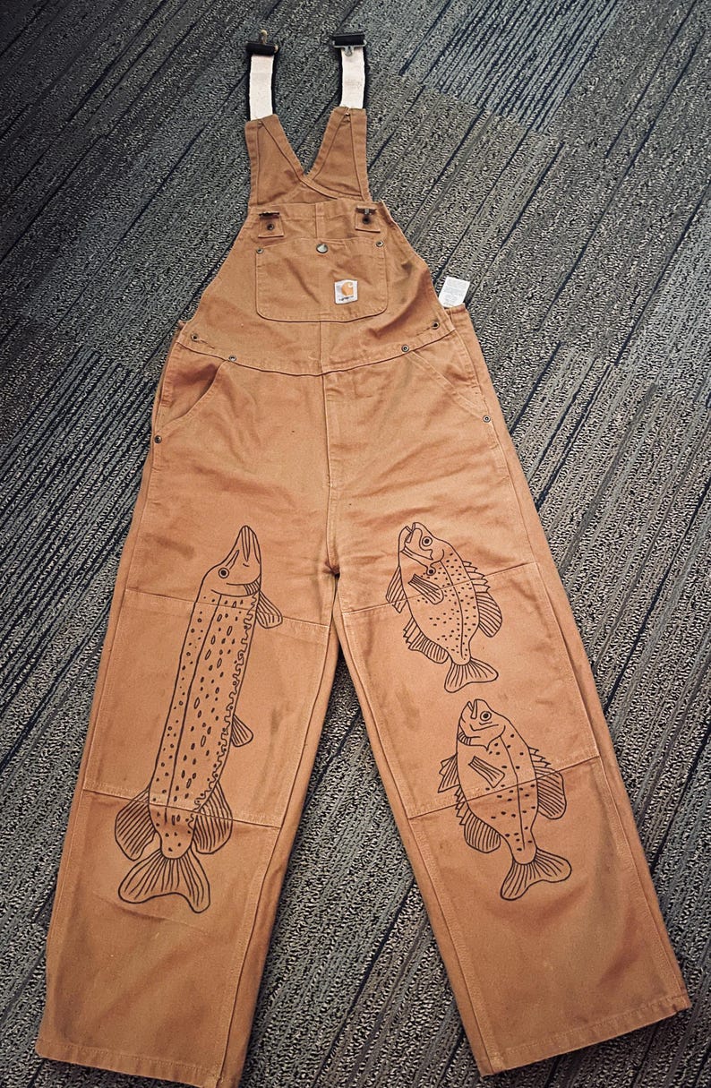 May include: Brown canvas overalls with a white strap and a black fish design on each leg.