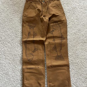 May include: Brown work pants with a fish design on each leg. The fish are outlined in black and are facing opposite directions.