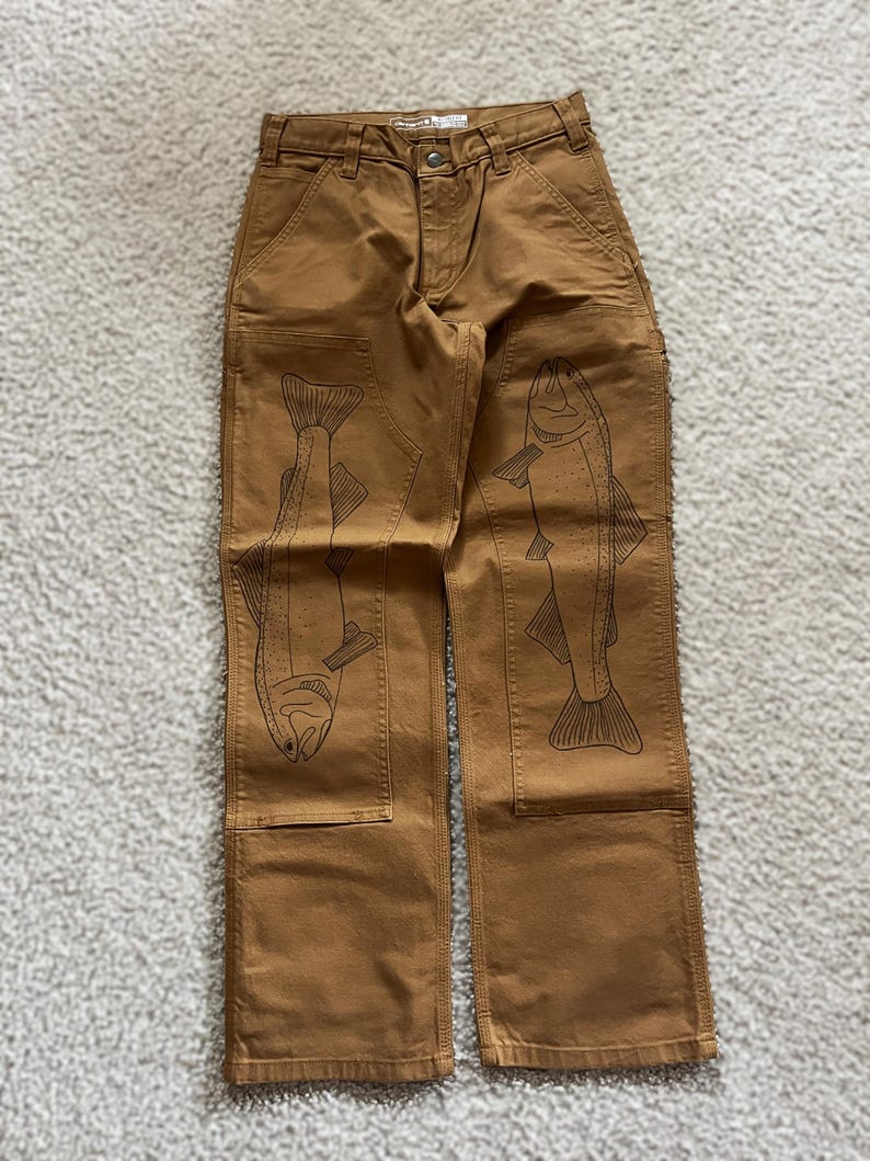 May include: Brown work pants with a fish design on each leg. The fish are outlined in black and are facing opposite directions.