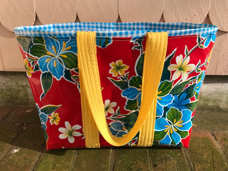 Puede incluir: Bolso tote rojo con estampado floral de flores azules, blancas y amarillas. Tiene asas amarillas y forro de cuadros vichy azul y blanco. El bolso est&aacute; hecho de un material duradero y es adecuado para transportar varios art&iacute;culos.