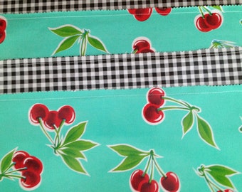 Manteles individuales reversibles de hule en un diseño retro de cerezas sobre verde espuma de mar.