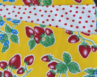 Manteles individuales reversibles de hule con estampado retro de fresas sobre fondo amarillo limón y lunares rojos.
