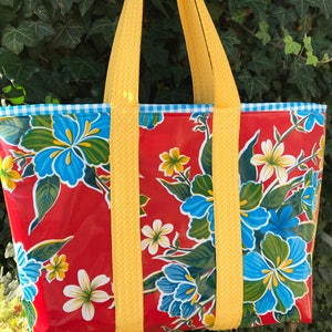 Puede incluir: Un bolso tote grande con un vibrante estampado floral. El bolso presenta un fondo rojo con flores azules y blancas y hojas verdes. Las correas amarillas y un ribete a cuadros azul y blanco completan el dise&ntilde;o. El bolso est&aacute; dise&ntilde;ado para transportar art&iacute;culos.