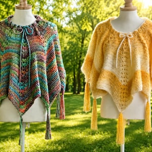 May include: Two handmade crochet ponchos on display. One is a vibrant mix of colors, including green, blue, orange, and red. The other is a warm yellow and white. Both have tassels and are displayed on mannequins.